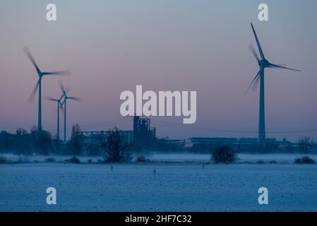 Im Industriegebiet Rothensee in Magdeburg drehen sich Windkraftanlagen, während die untergehende Sonne den Himmel verfärbt. Stockfoto