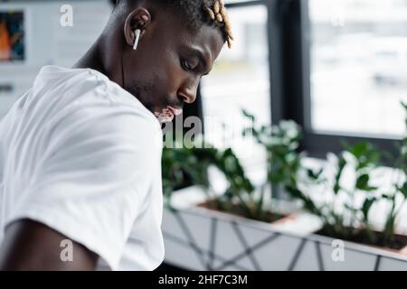 Junger afroamerikanischer Mann mit Vitiligo-Haut, der im Büro im Kopfhörer Musik hört Stockfoto