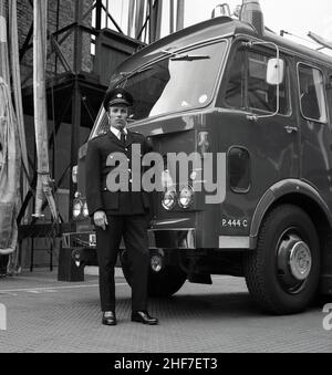 1960s, historisch, ein Stationsbeamter der Londoner Feuerwehr, der in seiner Uniform von einem Dennis-Feuerwehrmann in der Lewisham Fire Station, Southeast London, England, Großbritannien, stand. Die Brüder Dennis, John und Raymond, begannen 1895 mit der Herstellung und dem Verkauf von Fahrrädern, bevor sie zu Autos und Nutzfahrzeugen und dem legendären Feuerwehrauto weiterkamen. Stockfoto