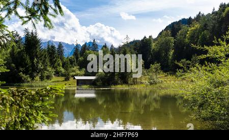Schmölzer See bei Garmisch-Partenkirchen mit Blick auf eine Bootshütte bei schönem Wetter, Bayern, Deutschland Stockfoto
