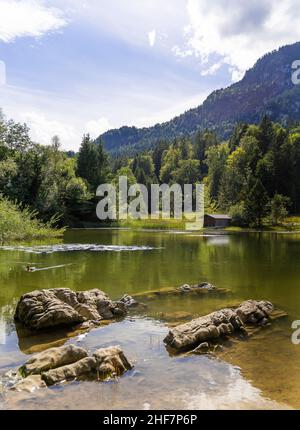 Schmölzer See bei Garmisch-Partenkirchen mit Blick auf eine Bootshütte bei gutem Wetter, Felsen im Vordergrund, große Steine ragen aus dem Wasser, Bayern, Deutschland Stockfoto