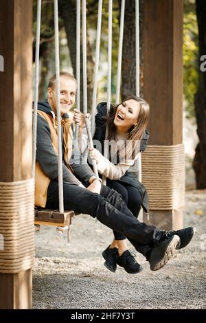 Seitenansicht eines fröhlichen, lachenden Paares, das auf einer Schaukel im Park im Freien sitzt. Hochwertige Fotos Stockfoto