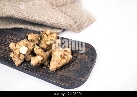 Jerusalemer Artischockenknollen liegen auf einem Holzbrett auf einem hellen Tisch. Speicherplatz Kopieren Stockfoto