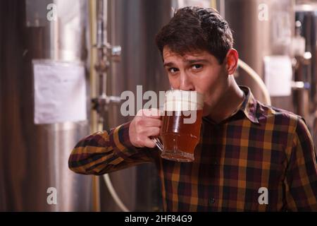 Mann schlürft köstliches Craft-Bier aus einem Becher und schaut zur Kamera Stockfoto