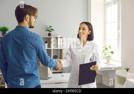 Freundliche Ärztin schüttelt sich die Hände mit ihrem Patienten im medizinischen Büro der modernen Klinik. Stockfoto