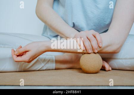 Unterarmmuskulatur myofasziale Freisetzung mit großer Kork-Massagekugel auf Kork-Yoga-Matte. Konzept: Selbstpflege zu Hause, nachhaltige Requisiten Stockfoto