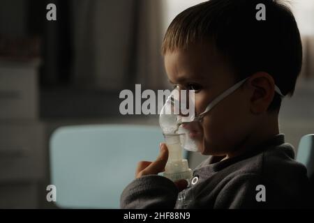 Behandlung zu Hause. Der Junge atmet mit einem Vernebler ein und inhaliert Medikamente in seine Lungen. Selbstbehandlung der Atemwege mit Inhalation. Stockfoto