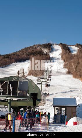 Skifahrer stehen am White Peaks Quad Sessellift im Skigebiet Waterville Valley in Waterville Valley, New Hampshire, USA, an. Stockfoto