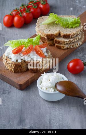 Roggenbrotscheiben mit Quark und Tomaten auf Holzplatte Stockfoto