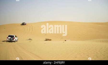 Luftaufnahme auf Offroad-Abenteuer mit SUV in der Arabischen Wüste bei Sonnenuntergang mit Skyline von Dubai oder Stadtbild. Wüstentouren mit SUV. Offroad-SUV beim Fahren Stockfoto