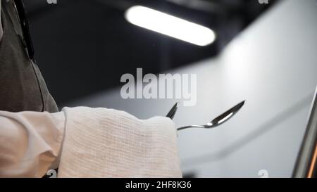 Nahaufnahme der Hände, die Besteck mit einem weißen sauberen Tuch abwischen. Ein Kellner polierte und trocknete Löffel für die Verpflegung. Stockfoto