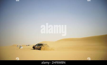 Luftaufnahme auf Offroad-Abenteuer mit SUV in der Arabischen Wüste bei Sonnenuntergang mit Skyline von Dubai oder Stadtbild. Wüstentouren mit SUV. Offroad-SUV beim Fahren Stockfoto
