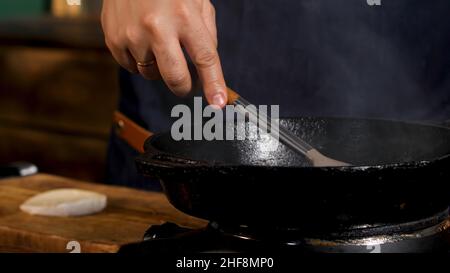 Nahaufnahme der männlichen Bratsoße und Zugabe von Zucker oder Salz in einer schwarzen Eisenpfanne. Prozess der Zubereitung von Speisen im Restaurant. Stockfoto