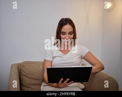 Lächelnde Frau, die auf ihr Tablet schaut, das auf der Couch liegt Stockfoto