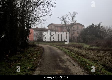 Landstraße mit einem Herrenhaus am Ende davon an einem nebligen Tag im Winter Stockfoto