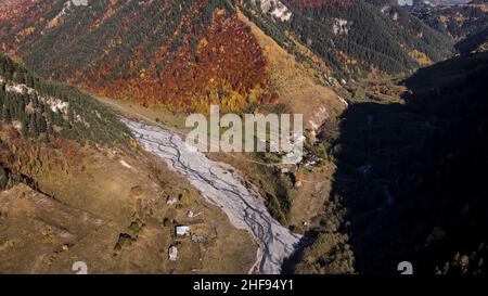 Luftaufnahme eines charmanten kleinen Dorfes im Tal in der Nähe von bewaldeten Hügeln. Fliegen Sie über die Berge, die von bunten Herbstbäumen bedeckt sind. Stockfoto