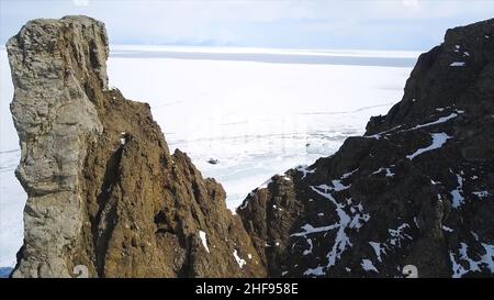 Luftaufnahme von erstaunlichen Klippen im Winter und dem endlosen gefrorenen See. Natürliche Landschaft mit Felsen am bewölkten Himmel und eisigen Wasseroberfläche backgro Stockfoto