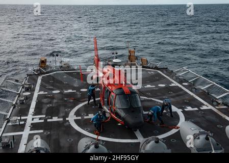 Mitglieder der Küstenwache an Bord des USCGC Stratton (WMSL 752) führen Verzurrungsoperationen mit einem MH-65E Dolphin-Hubschrauber im Pazifischen Ozean durch, 29. Dezember 2021. Die Crew von Stratton führte Flugoperationen durch, um die operativen Fähigkeiten aufrechtzuerhalten und die Bereitschaft zu erhöhen. (USA Foto der Küstenwache des U.S. Marine Corps Sgt. Sarah Stegall) Stockfoto