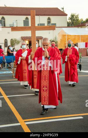 Im Rahmen einer Messe im Freien, bilden multirassisch getragente Priester eine Prozession, während sie ein Kreuz vor ihrer Gemeinde auf dem Parkplatz eines Southers laufen Stockfoto