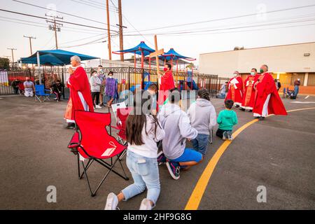 Im Rahmen einer Messe im Freien, bilden multirassisch getragente Priester eine Prozession, während sie ein Kreuz vor ihrer Gemeinde auf dem Parkplatz eines Southers laufen Stockfoto