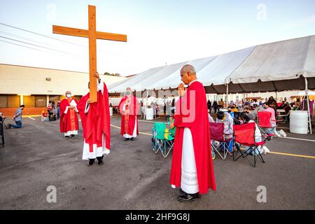 Im Rahmen einer Messe im Freien, bilden multirassisch getragente Priester eine Prozession, während sie ein Kreuz vor ihrer Gemeinde auf dem Parkplatz eines Southers laufen Stockfoto