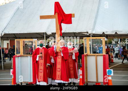 Im Rahmen einer Messe im Freien, bilden multirassisch getragente Priester eine Prozession, während sie ein Kreuz vor ihrer Gemeinde auf dem Parkplatz eines Southers laufen Stockfoto