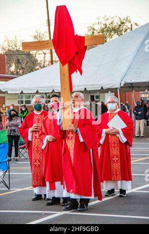 Im Rahmen einer Messe im Freien, bilden multirassisch getragente Priester eine Prozession, während sie ein Kreuz vor ihrer Gemeinde auf dem Parkplatz eines Southers laufen Stockfoto