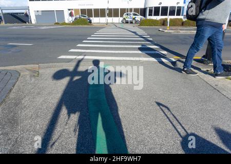 Auckland Neuseeland - Juli 12 2018; Schatten von Reisenden, Taschen und Beinen am Flughafen mit Polizeifahrzeug über Fußgängerüberweg. Stockfoto