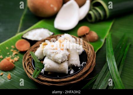 Kue Putu, traditioneller indonesischer Kuchen aus Reismehl, Palmzucker, Pandan-Blatt und zerkleinerten Kokosnuss. Kommt mit Zylinderform mit Bambusrohr Stockfoto