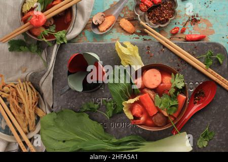 Würzige thailändische Tom Yum-Suppe mit Meeresfrüchten, serviert auf einer rustikalen braunen Schüssel auf grünem Holzhintergrund Stockfoto