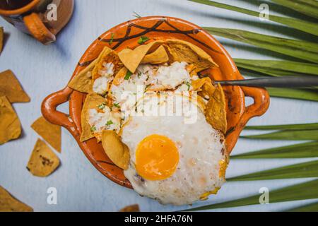 Tontopf mit Chilaquiles mit Spiegelei auf der Oberseite und über der weißen Oberfläche Stockfoto