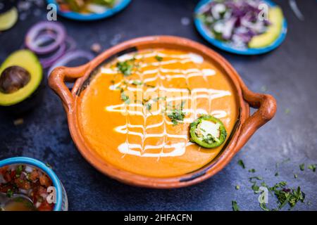 Köstliche Suppe im traditionellen Tontopf über dunkler Oberfläche Stockfoto