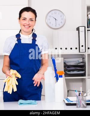 Frau, die das Büro mit Reinigungskräften, Handschuhen und Wischmopp putzt Stockfoto