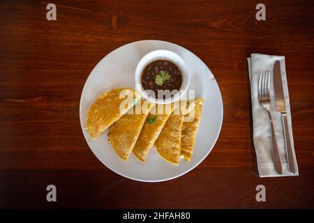 Teller mit traditionellen Quesadillas und Tasse Bohnen auf braunem Tisch Stockfoto