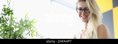 Blond in einem weißen Kleid sitzt vor einem Laptop Stockfoto