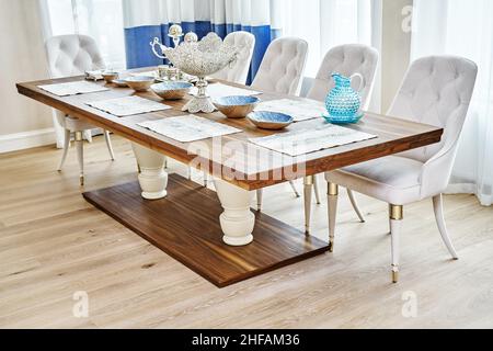 Luxuriöser Vintage-Esstisch aus massivem Nussbaum- und Furnierholz mit festlichem Ambiente und Sesseln in der Nähe des Fensters in einem geräumigen Zimmer Stockfoto