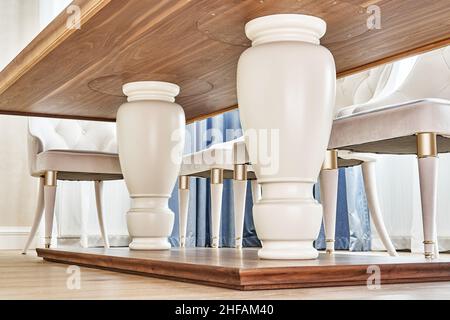 Massive, weiße Beine eines luxuriösen Vintage-Esstisches mit einer Oberfläche aus massivem Nussbaum- und Furnierholz und Stühlen in hellem Raum in Nahaufnahme Stockfoto