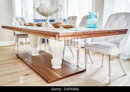 Luxuriöser Vintage-Esstisch aus massivem Nussbaum- und Furnierholz mit festlichem Ambiente und Sesseln in der Nähe des Fensters in einem geräumigen Zimmer aus nächster Nähe Stockfoto