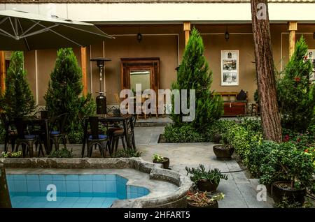 Isfahan, Nor Julfa, Iran, 16, November, 2021: Gemütliche Terrasse mit Tischen und Stühlen zwischen Nadelbäumen und Blumen auf dem Gebiet des Hotels 'Arme Stockfoto