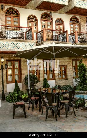 Tisch und Stühle unter einem Baldachin in der Nähe des Pools mit einem Brunnen inmitten der Blumen im Hofgarten des Hotels 'Armenia' im armenischen Viertel Stockfoto