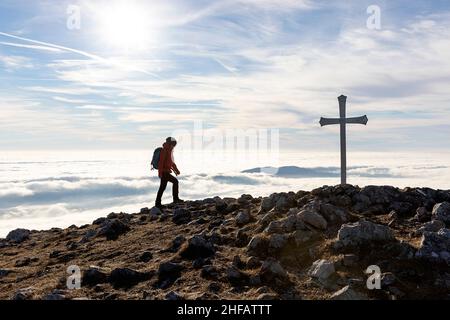 Frau, die zum Kreuz auf dem Gipfel des Kucelj-Berges geht, über dem Nebel im Vipava-Tal, Slowenien Stockfoto