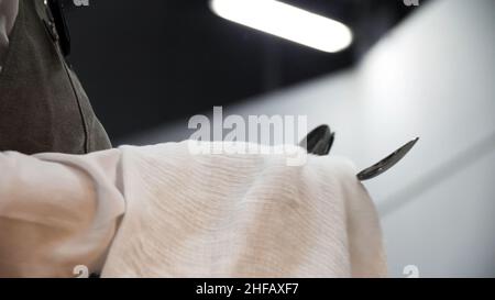 Nahaufnahme der Hände, die Besteck mit einem weißen sauberen Tuch abwischen. Ein Kellner polierte und trocknete Löffel für die Verpflegung. Stockfoto