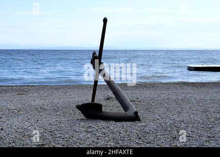 Großer schwarzer Eisenanker, der als Touristenattraktion aus dem Wasser am Kiesstrand gelegt wurde Stockfoto