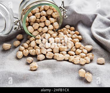 Ungekochte getrocknete Kichererbsen im Glas auf grauem Textilhintergrund Stockfoto