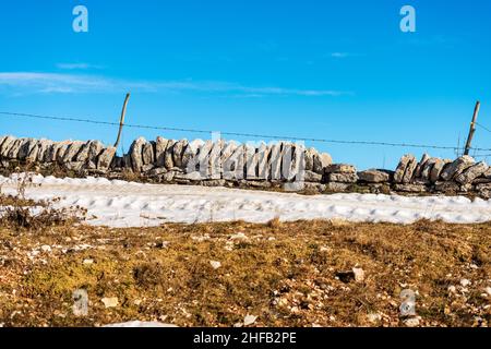 Zaun aus Trockensteinmauer und Stacheldraht, der zur Abgrenzung von Weide- und Kulturfeldern im Regionalen Naturpark Lessinia-Plateau, Italien, verwendet wird. Stockfoto