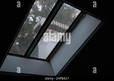 Ein Fenster aus Dach, Glas auf dem Dach aus Glas und architektonische Figur hinter Zaun. Stockfoto