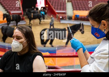München, Deutschland. 15th Januar 2022. Die Vaccinologin Caroline Klima impft Thomas Frauendorfer im Circus Krone gegen das Corona-Virus, während Pferde im Ring im Hintergrund trainieren. Kredit: Lennart Preiss/dpa/Alamy Live Nachrichten Stockfoto