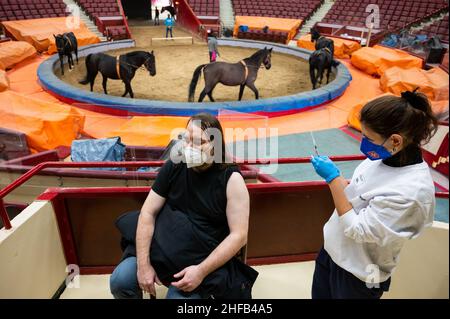 München, Deutschland. 15th Januar 2022. Die Vaccinologin Caroline Klima impft Thomas Frauendorfer im Circus Krone gegen das Corona-Virus, während Pferde im Ring im Hintergrund trainieren. Kredit: Lennart Preiss/dpa/Alamy Live Nachrichten Stockfoto