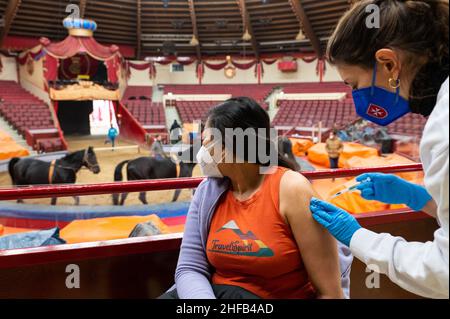München, Deutschland. 15th Januar 2022. Die Vaccinologin Caroline Klima (r) impft im Circus Krone Paitul Supaporn gegen das Corona-Virus, während Pferde im Hintergrund im Ring trainieren. Kredit: Lennart Preiss/dpa/Alamy Live Nachrichten Stockfoto