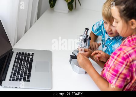 Erneuerbare Energien, Kinder, Technologie, Wissenschaft und Menschen Konzept - Kinder oder Freunde mit Laptop-Computer und Mikroskop-Modell Stockfoto